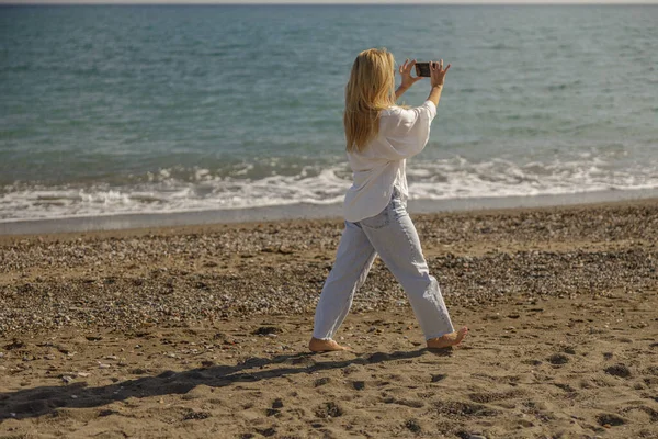 Full length shot of woman recording video using smartphone while having a walk along the sea coast — Foto de Stock