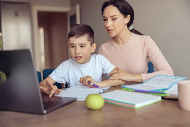 Bilgisayarın önünde annesi olan küçük bir çocuğun evinden ders çalışıyor. Okullar.