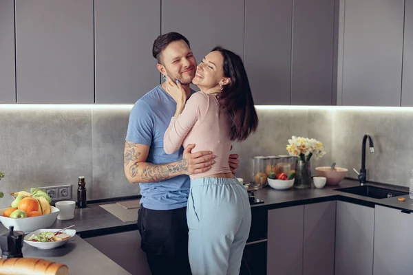 Cheerful just-married young Caucasian couple in hugs having fun and laughing in kitchen. — стокове фото