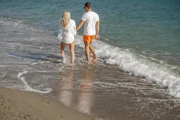 Romantic couple holding hands while having romantic time together, walking in waves on beach vacation — стоковое фото