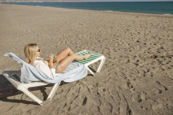 Mayolu kadın kokteyl içiyor, iskemlede dinleniyor, güneşli plaj gününün tadını çıkarıyor.