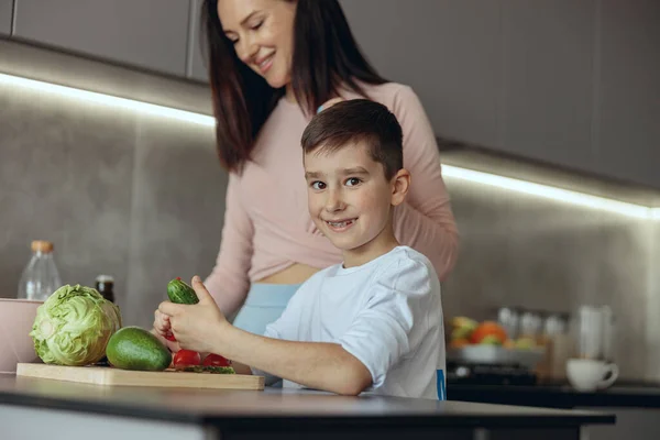 Portrait of happy Caucasian small boy smiling and cooking vegetables with mommy at home. — Foto de Stock