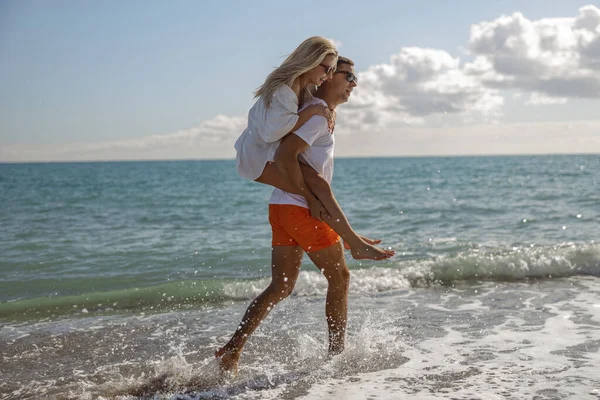 Man giving woman piggyback ride while walking together along the sea coast — Stok Foto