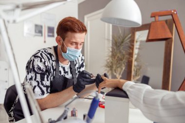 Genç manikürcü müşteriyle güzellik salonunda çalışıyor.