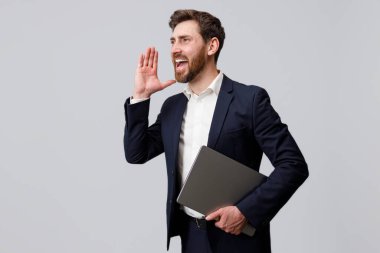 Bağıran iş adamı dizüstü bilgisayarını tutuyor ve gri stüdyonun arka planına bakıyor.