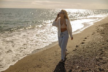 Deniz kıyısında telefonda konuşurken gülümseyen mutlu bir bayan.