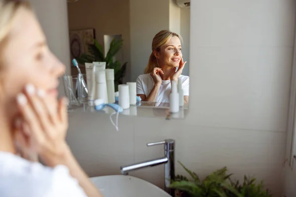 Refleksi wanita cantik berambut pirang di cermin di kamar mandi. Tutup. Rutinitas perawatan kulit. — Stok Foto