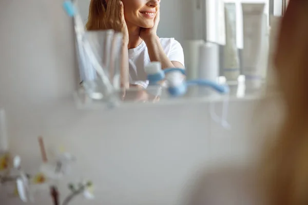 Menutup dagu perempuan dan tersenyum di cermin di kamar mandi. Konsep perawatan kulit yang sempurna. — Stok Foto