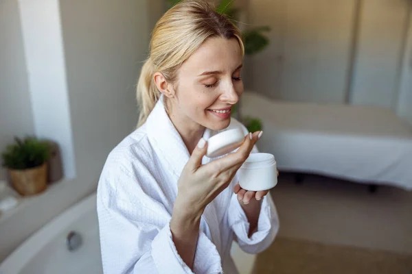 Atraente jovem caucasiano feminino cheirando creme facial ou loção corporal no banheiro. — Fotografia de Stock