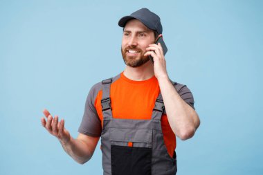 Üniformalı teslimatçı mavi stüdyoda cep telefonuyla konuşuyor.