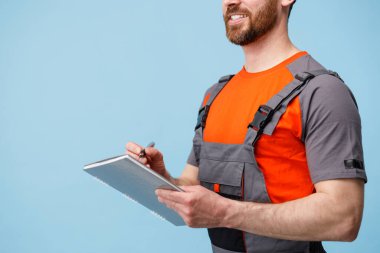 Üniformalı bir erkek kuryenin tableti eline alıp iş notları alması.