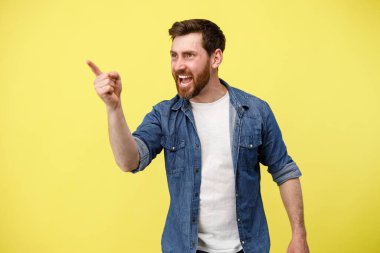 Gülümseyen ve sakallı yakışıklı adam sarı arka planda dikilirken parmağını işaret ediyor.