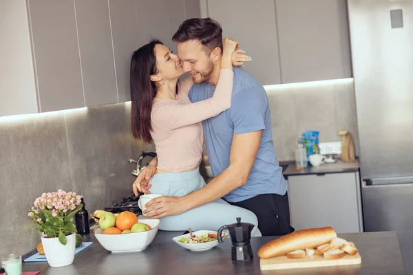 Cheerful Caucasian man and woman in love hugging in kitchen in the morning. Having coffee. — Stock Photo, Image