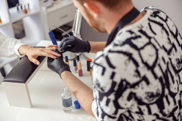 Back view of nail technician in black protective gloves doing manicure for woman in nail art studio