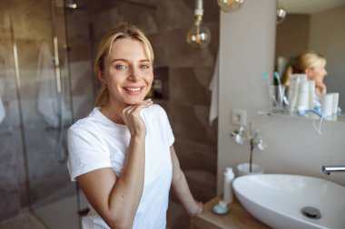 Beyaz saçlı güzel bir kadının gülümseyen ve banyoda ayakta duran portresi. Dikkat.