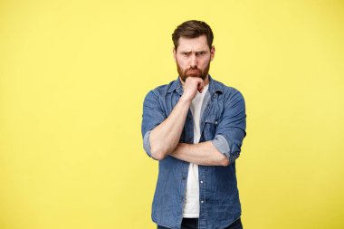 Ciddi bir adamın stüdyo portresi sarı arka planda sakallı bir şekilde el ele tutuşuyor.