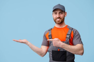 Teslimatçı mavi arka planda duruyor. Parmağını boş bir yerde gösteriyor. Stüdyo çekimi