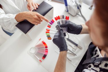 Modern manikür stüdyosunda kadın müşterinin tercih ettiği tırnak cilasını parlak bir açıdan seçmesi.