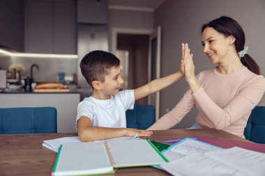 Küçük beyaz çocuk güzel mutlu annesine beşlik çakıyor. Evde ders çalışıyorum. Ev ödevi bitti..
