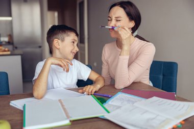 Güzel genç anne eğleniyor, küçük oğlunu güldürüyor, kalemle alay ediyor. Evde eğitim.