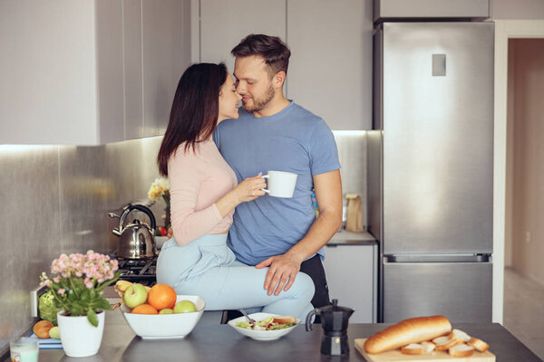 Caucasian young happy couple hugging and having coffee in morning on weekend. Love concept. Feelings