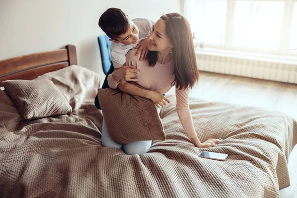 快乐快乐的高加索妈妈和年幼的儿子抱着孩子在卧室里玩耍 — 图库照片