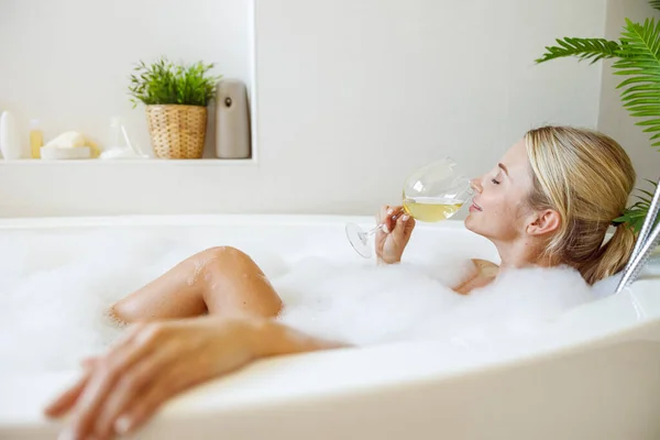 泡と白ワインをすすりながらお風呂でリラックスした若い白人女性 サイドビュー — ストック写真