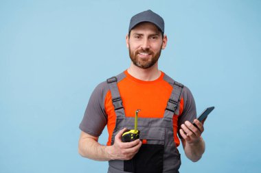 Üniformalı bir adam cep telefonuyla konuşuyor ve elinde mavi stüdyonun arka planında mezura var.. 