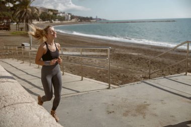 Spor giyimli mutlu bir kadın, deniz kıyısında koşarken formda ve yağlı.