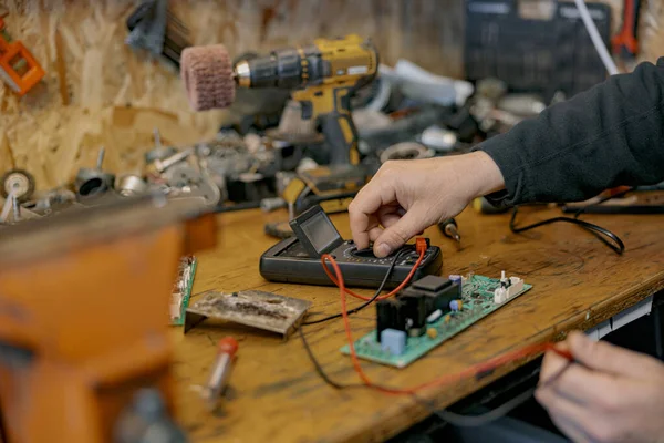 Close up of electrician hands checks electrical voltage on the circuit board with device in workshop