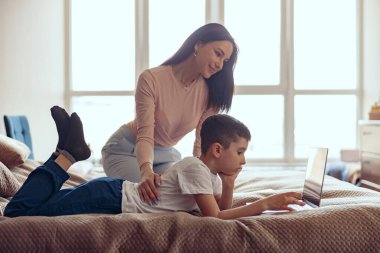 Küçük tatlı oğlu olan güzel beyaz bir kadın bilgi aramak için dizüstü bilgisayar kullanıyor. Dinleniyor.