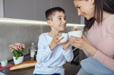 Güzel bir anne ve küçük bir çocuk ellerinde fincanlarla birbirlerine gülümseyerek ve sevgiyle bakıyorlar. Portre.