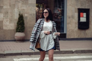 Neşeli, mutlu, güneş gözlüklü ve şık elbiseli güzel bir kadın şehirde yürüyor. Şehirde moda..