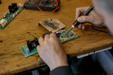 Tamirci ellerinin kapatılması atölyedeki masanın üzerindeki elektronik cihazın devre levhasını lehimliyor.