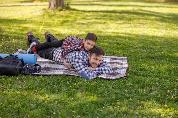 快乐的年轻父亲躺在公园里 小儿子躺在爸爸的背上 放松与孩子 — 图库照片