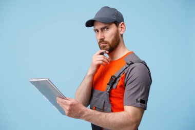 Üniformalı teslimatçı özenle sakalına dokundu. Elinde mavi atölyenin arka planında tablet vardı.