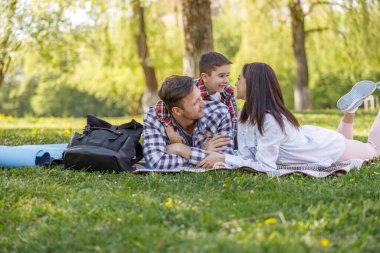 Kafkasyalı ebeveynler yeşil ormanda çimlerin üzerinde yatıyorlar ve günlerini küçük oğluyla geçiriyorlar. Hafta sonu aile