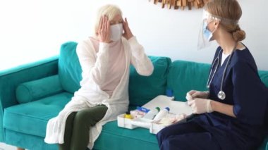 Ev ziyareti sırasında koruyucu maskeli emekli bir kadının vücut ısısını dijital termometreyle ölçen güvenlik görevlisi.