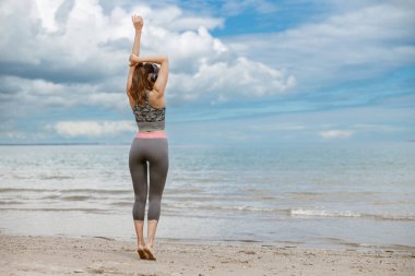 Sahilde esneme egzersizleri yapan kulaklıklı bir kadın. Sağlıklı ve aktif yaşam konsepti