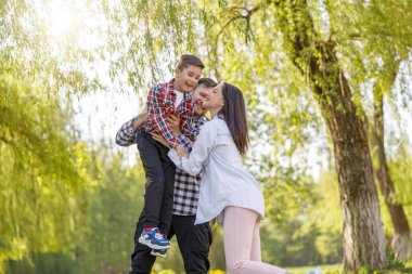 Cheerful happy man and woman with cute small son sitting on dads shoulders and hugging. Portrait.