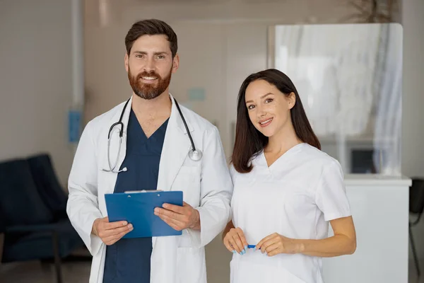Portrait of doctor and nurse standing near reception in hospital and looking camera. High quality photo