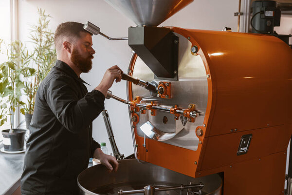 Business owner operating a modern coffee bean roasting machine in small coffee factory