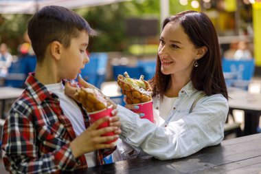 Genç, güzel bir anne ve parkta tatlı waffle yiyen tatlı bir oğul. Fast food . Çocuklu kadın.