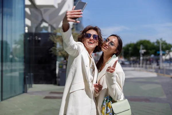 Moda kıyafetleri içindeki kadınlar iş merkezinin yakınında selfie çekiyorlar. Bulanık arkaplan