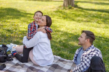 Mutlu güzel anne kucaklaşması ve küçük oğlunla gurur duyması. Ailesi piknikte olan bir adam. Park yerinde..