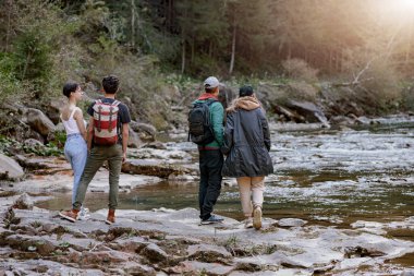 Back view on two couples at rocky fast mountains river standing hand in hand and enjoying view. Rear