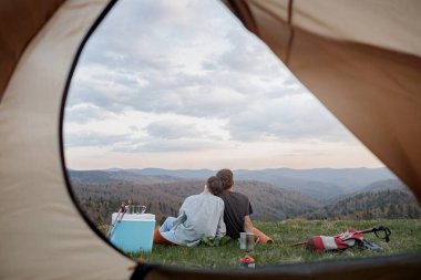 View from inside tent on couple in love hugging, resting on peak of mountain. Beautiful nature. Rear