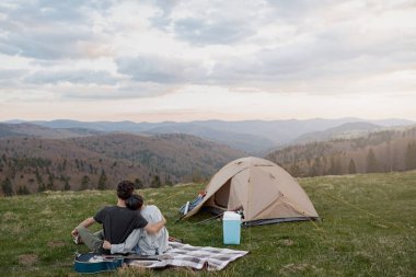 Rear on couple hugging and resting in mountains. On peak of mount, Beautiful view. Together. Rear.