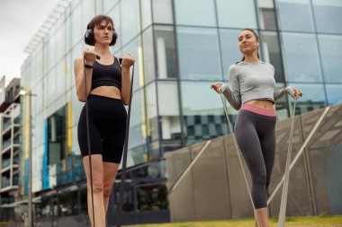 Kadınlar şehirde bacak kaslarını spor lastiğiyle eğitir. Açık hava antrenmanı. Sağlıklı yaşam tarzı