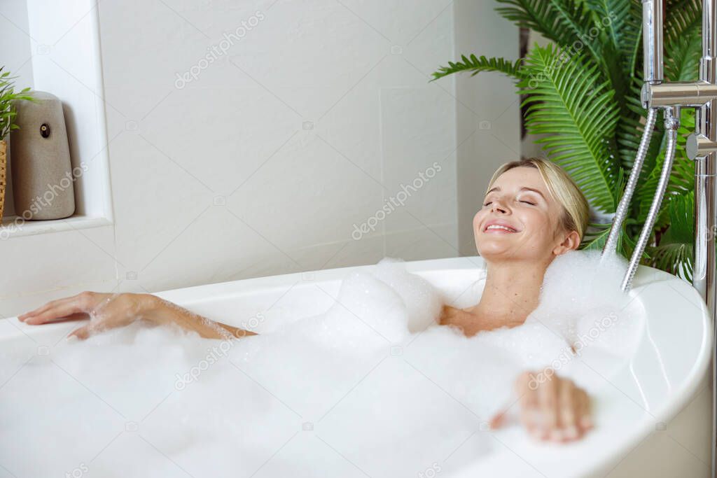 Attractive Caucasian young female enjoying bubbles, relaxing and taking bath in morning. Spa day.